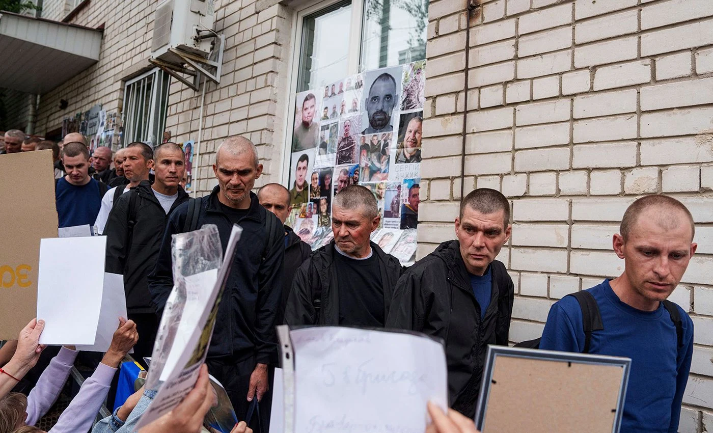 Українські солдати йдуть повз людей із фотографіями своїх зниклих родичів після повернення з полону внаслідок обміну військовополоненими між Росією та Україною в Чернігівській області, Україна, 24 травня 2025 року. Фото: Evgeniy Maloletka / AP